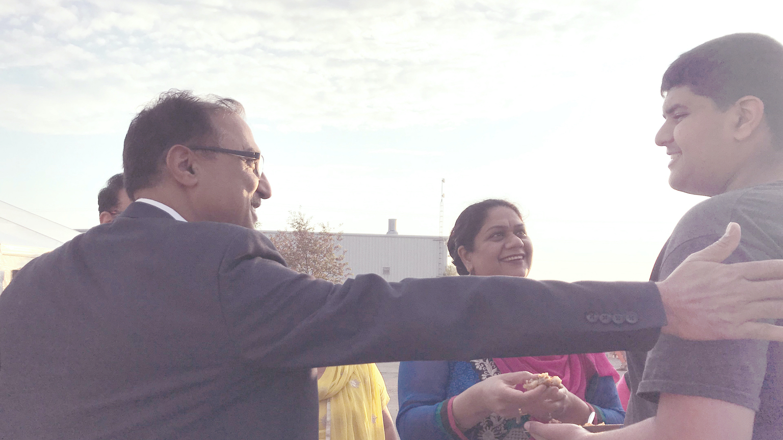An image of Amarjeet Sohi reaching out and touching a young man's shoulder while a woman looks on, smiling.