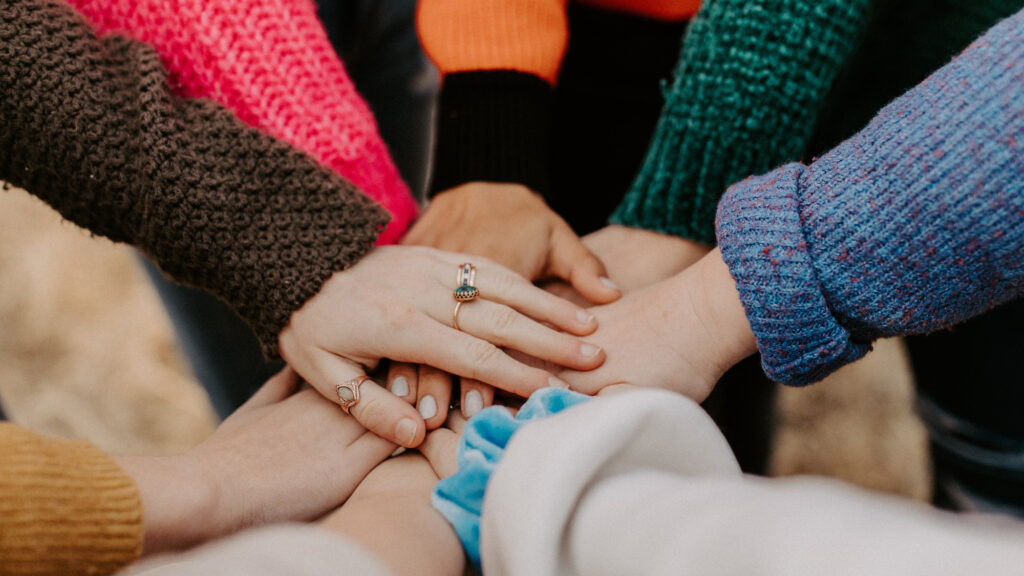 An image of eight hands from eight people in the middle of a circle on top of one another