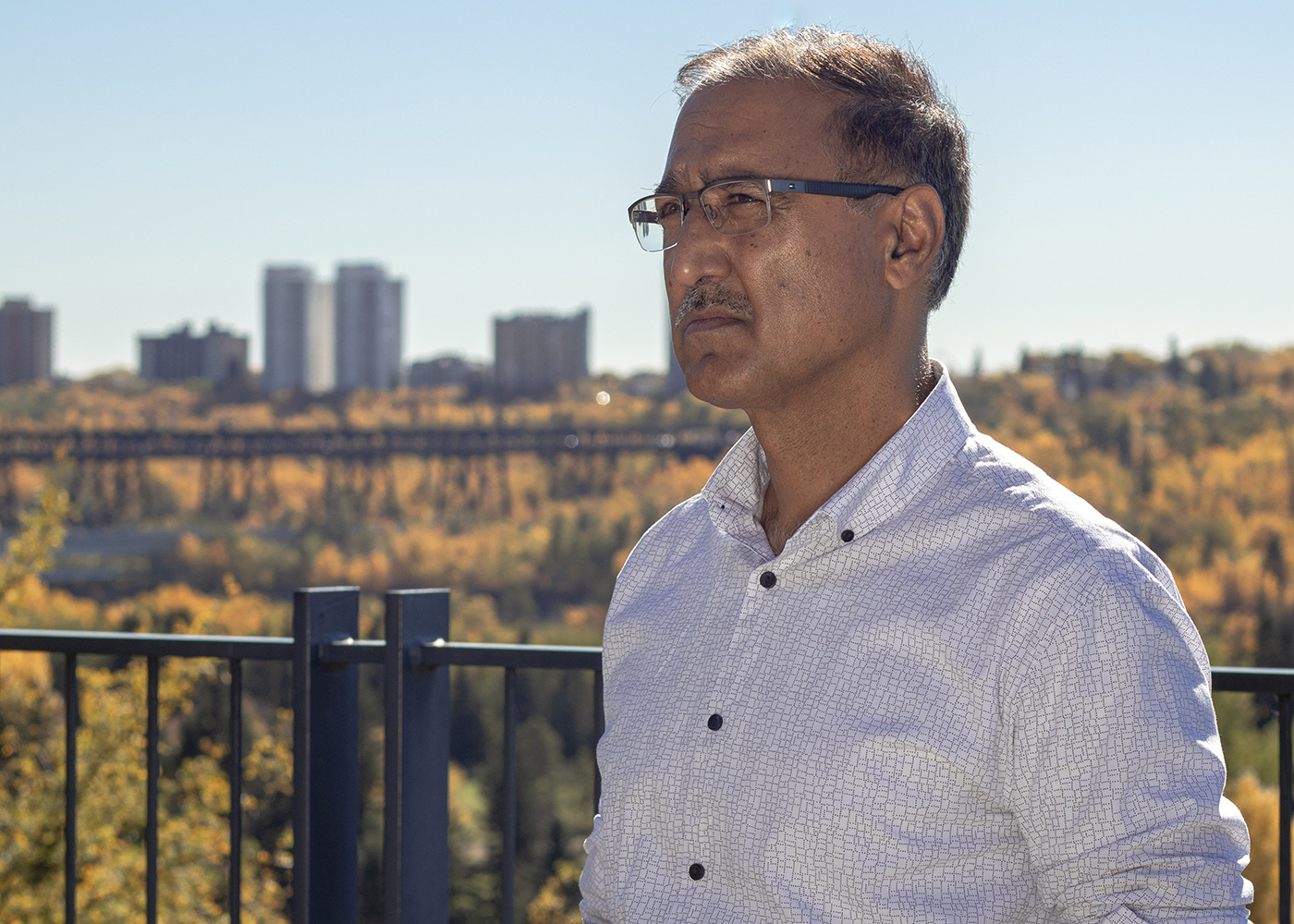 Amarjeet Sohi standing atop the Edmonton river valley. You can see the outline of the High Level Bridge in the background.